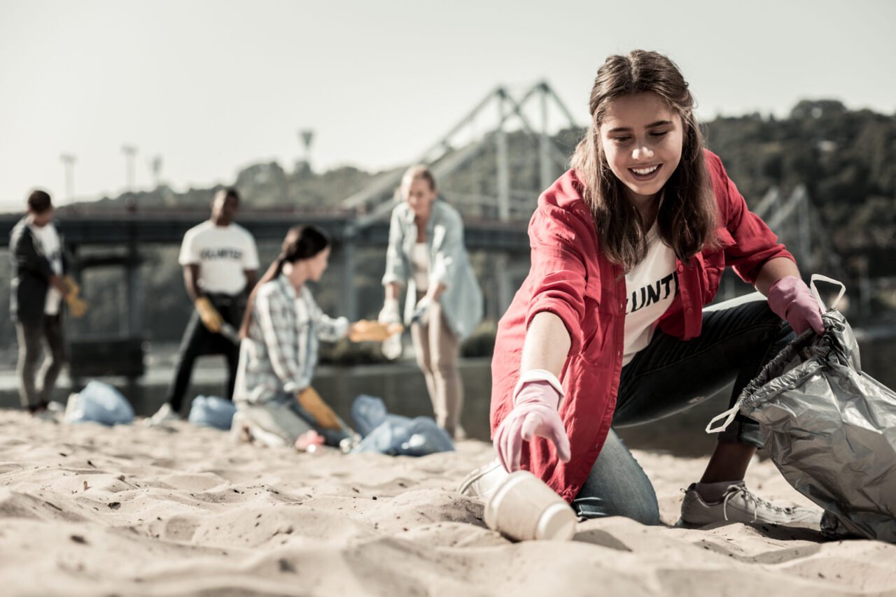 Home young dark haired student wearing red anorak putting cups into garbage bag